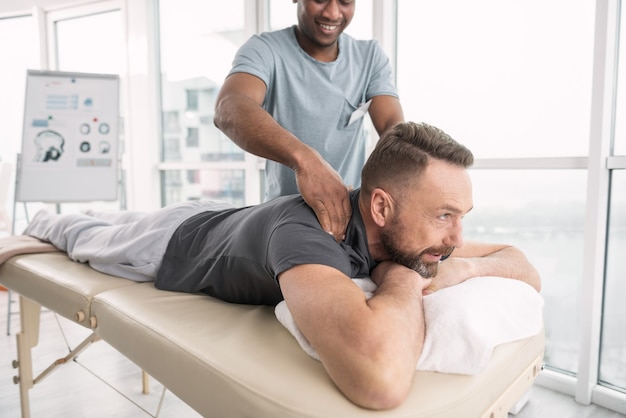 Massage thérapeutique. Joyeux bel homme barbu souriant tout en profitant du massage thérapeutique