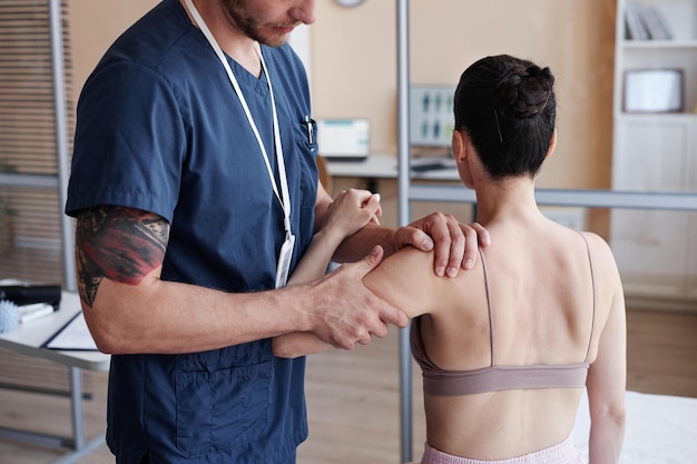 Massagiste en uniforme examinant le corps du patient avant la procédure de massage à l'hôpital