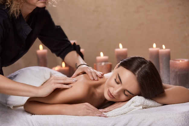 Photo masseur faisant un massage pour le dos de la femme dans un salon spa avec de nombreuses bougies