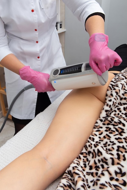 Le masseur fait un massage à l'aide d'une machine de massage anticellulite avec technologie de compression et de vibration dans le bureau de l'esthéticienne