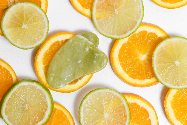 Un masseur de gouache verte repose sur des tranches rondes d'orange et de citron vert sur un fond blanc recouvert de gouttes d'eau pour votre conception