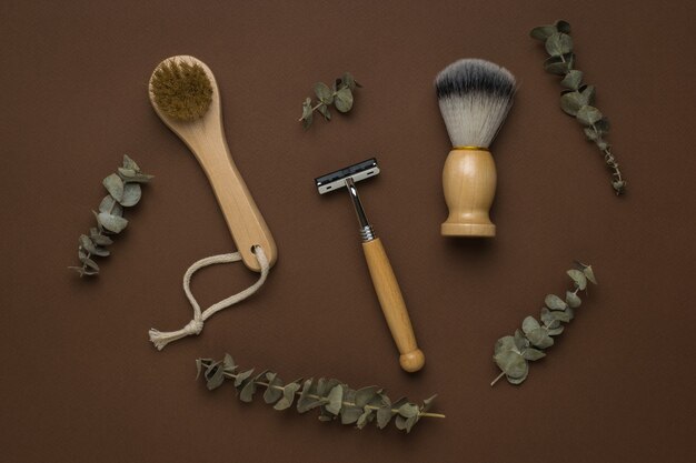 Masseur à main et accessoires de rasage avec branches d'eucalyptus sur fond marron. Mise à plat.