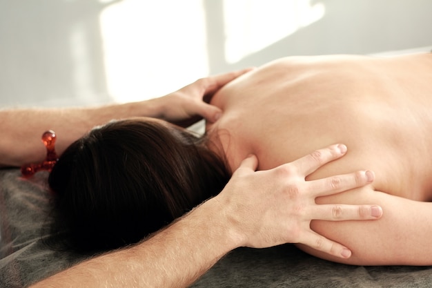 Un masseur masculin effectue des soins de spa pour une jeune femme allongée sur le ventre sur un canapé