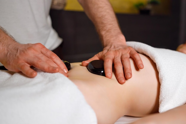 Masseur massant l'abdomen de la femme avec des pierres de lave