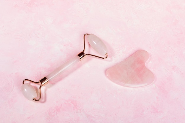 Masseur en pierre de quartz rose pour le visage et grattoir Guasha sur fond rose Vue de dessus Espace de copie