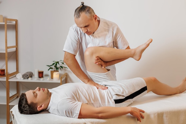 Masseur thérapeute fort et concentré en uniforme faisant de la thérapie manuelle pour sportif