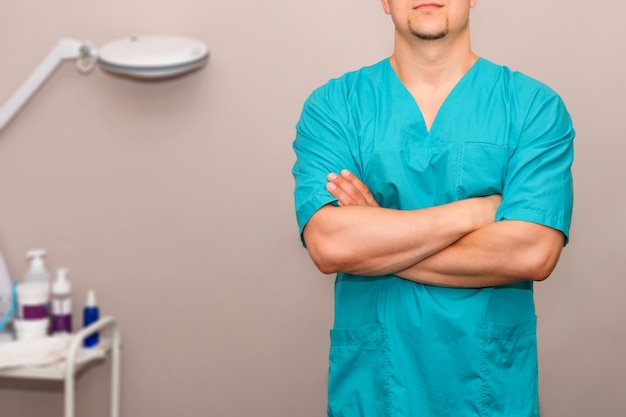 Masseur en uniforme avec les bras croisés debout à une table de massage en clinique.