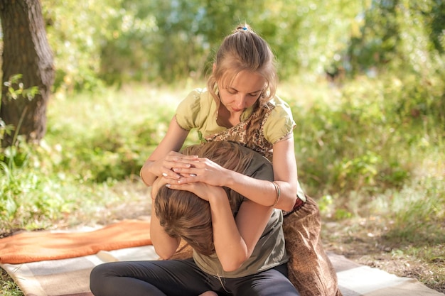 Une masseuse expérimentée masse soigneusement une fille sur l'herbe.