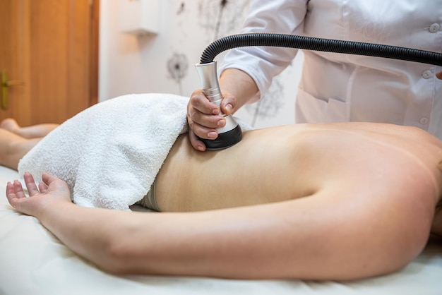 Une masseuse professionnelle effectue un traitement de la cellulite sur tout le corps avec un appareil spécial