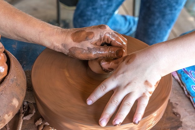 Master class en poterie Un potier apprend à un enfant à faire des plats à partir d'argile rouge