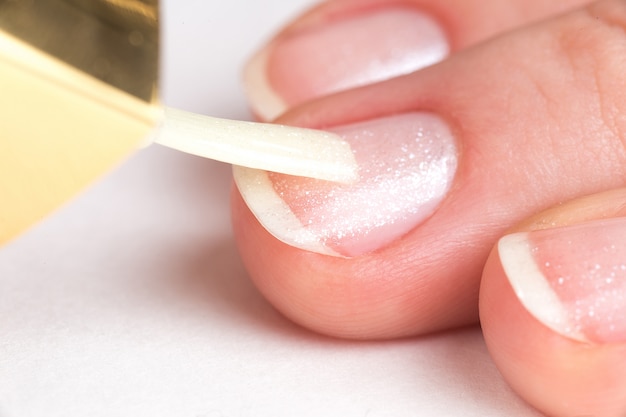 Master of manucure couvre les ongles des clients vernis clair avec des étincelles