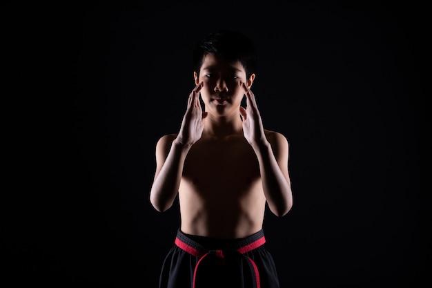 Master Red Black Belt TaeKwonDo Karaté garçon qui est athlète jeune adolescent montrent des poses de combat traditionnelles en tenue de sport, mur noir isolé copie espace, faible exposition à l'obscurité