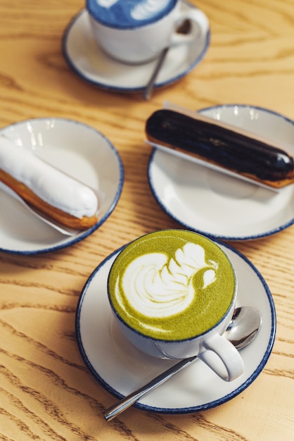 Matcha bleu et vert dans des verres sur une table en bois dans un café à côté d'un dessert sucré. Eclairs avec ganache au chocolat et glaçage avec différentes garnitures