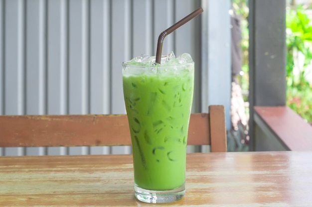 Matcha latte glacé ou thé vert au lait condensé en verre transparent avec paille noire sur table en bois servi au café