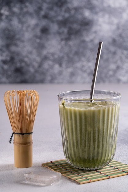 Matcha latte avec mousse à la crème dans des verres, fouet en bambou tusaku et poudre de matcha sur table en bois.