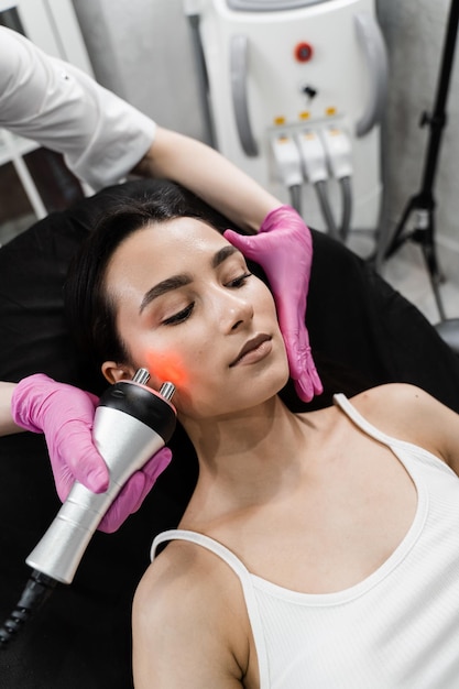 Photo matériel thermique ou radiofréquence lifting rf pour lisser les rides améliorant le teint et la turgescence de la peau resserrement et rajeunissement de la peau du visage de la fille lors de la procédure de cosmétologie