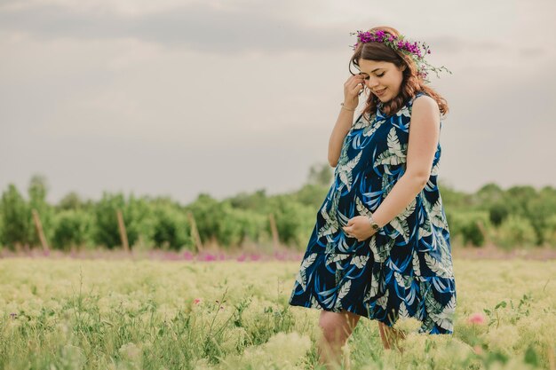 Maternité et grossesse Jeune femme enceinte touchant son gros ventre dans un champ plein de fleurs sauvages et se sentant heureuse