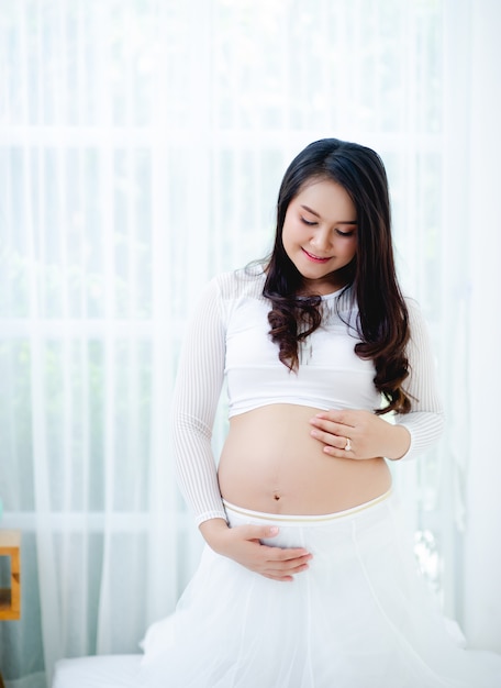 La maternité profite du bébé dans le ventre dans une robe blanche et une chambre blanche.