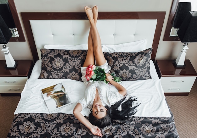 Matin d'une belle femme à l'hôtel avec des roses au lit
