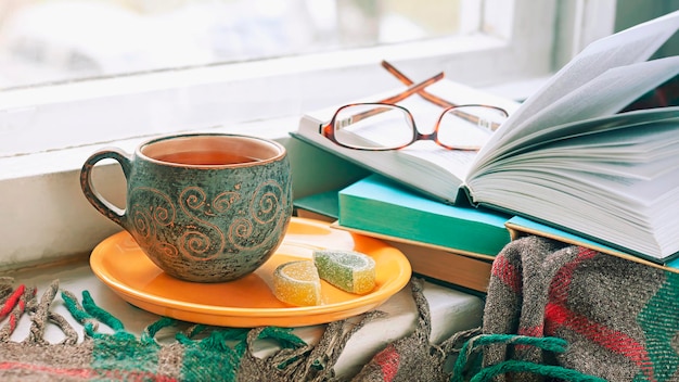 Matin confortable à la maison Une tasse de thé, une couverture de vieux livres et des verres sur le rebord de la fenêtre