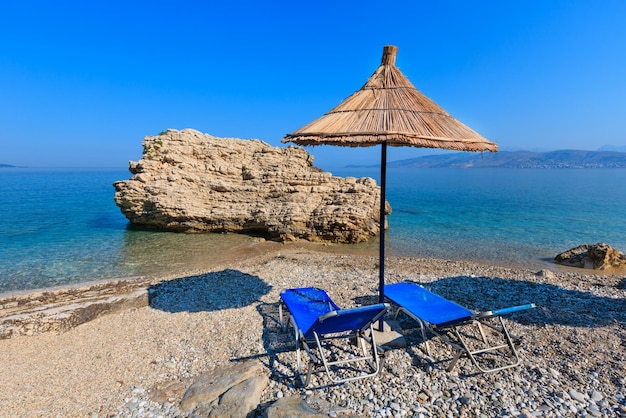 Matin d'été plage de Pulebardha avec transats et parasol paille (Saranda, Albanie).