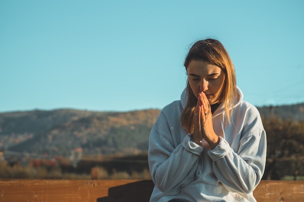 Le matin, la fille ferma les yeux, priant à l'extérieur, les mains jointes dans le concept de prière pour la foi, la spiritualité et la religion. Concept de paix, d'espoir, de rêves.