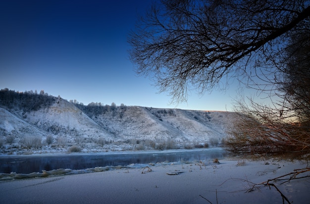 Matin glacial d'hiver avant l'aube. Rivière gelée depuis les rives vallonnées et les grandes banquises.