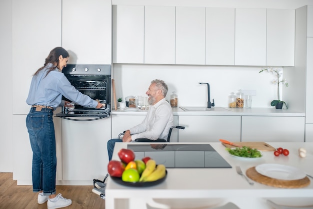 Matin à la maison. Homme handicapé aux cheveux gris et sa jeune femme dans la cuisine préparant le petit-déjeuner