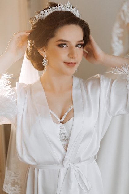 Le matin de la mariée avant le mariage une belle jeune femme avec un voile et une belle coiffure dans une robe blanche dans une pièce avec un intérieur merveilleux beauté naturelle et maquillage professionnel