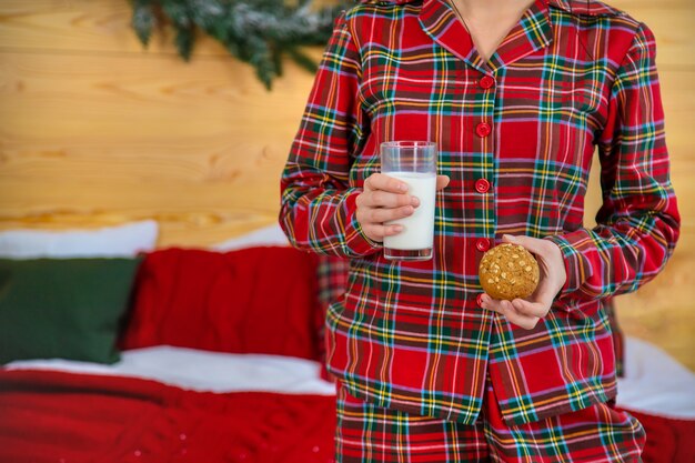 Matin de Noël, femme en pyjama avec des biscuits et un verre de lait. Mise au point sélective.