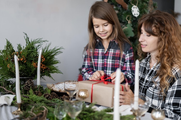 Le matin de Noël, maman donne à sa fille une boîte avec un cadeau à la table de fête La fille détache le ruban du cadeau du Nouvel An de sa mère Concept pour Noël et le Nouvel An à la maison