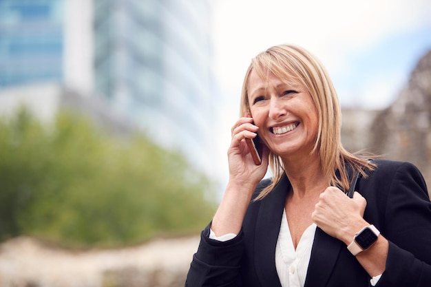 Mature Businesswoman Talking On Mobile Phone alors qu'elle se promène dans la rue de la ville