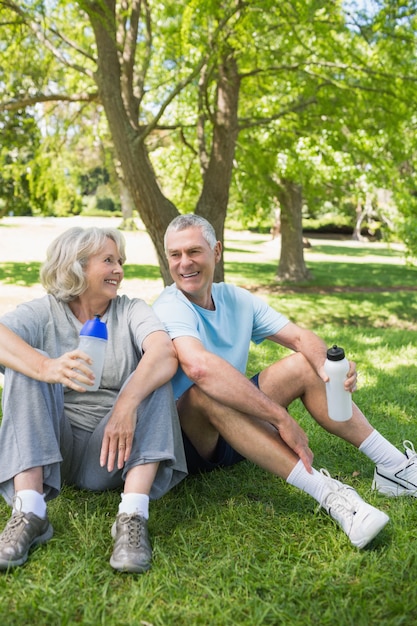 Mature couple assis avec des bouteilles d&#39;eau au parc