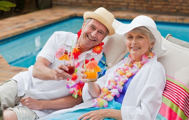 Mature couple buvant un cocktail au bord de la piscine