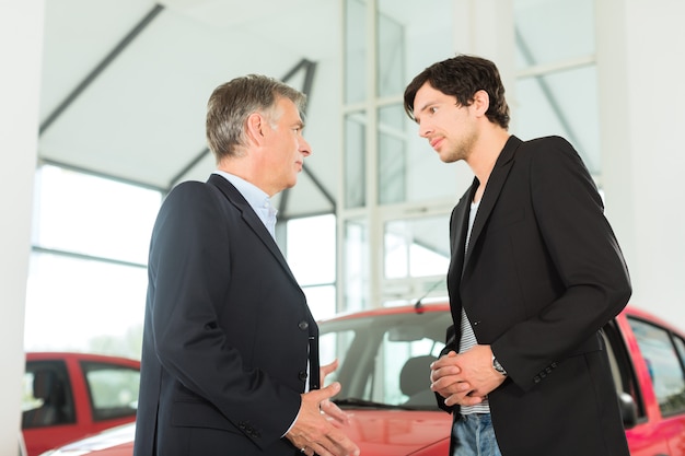 Mature dealer et jeune homme avec auto chez un concessionnaire automobile