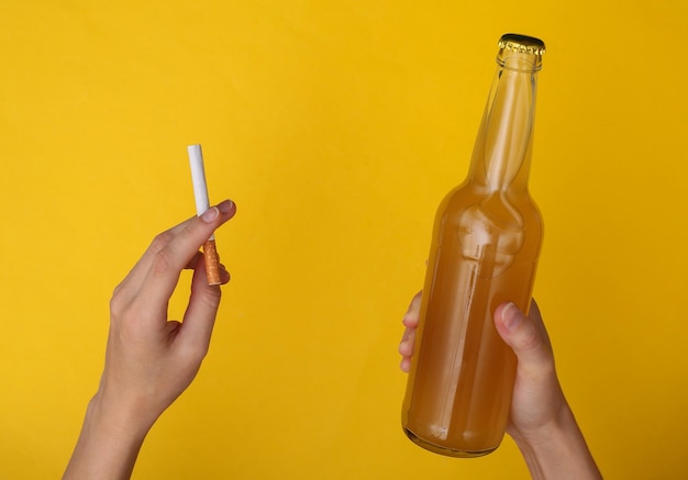 Mauvaises habitudes, dépendance à l'alcool et à la nicotine. Mains tenant une cigarette et une bouteille de bière sur fond jaune