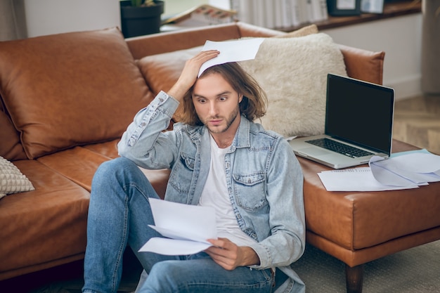 Mauvaises nouvelles. Jeune homme en chemise de jeans tenant des papiers et à la frustration