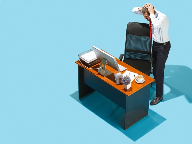 Mauvaises nouvelles. Vue ci-dessus d'un homme d'affaires travaillant sur un ordinateur portable. Jeune homme frustré en détresse debout à table de bureau. Entreprise, concept de lieu de travail. Émotions humaines, concepts d'expressions faciales. Studio bleu