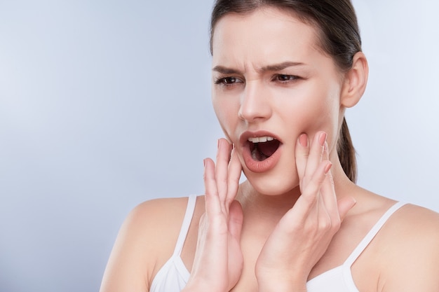 Maux de dents, dents blanches. Tête et épaules de jeune femme souffrant de maux de dents, problèmes de soins dentaires. Expression douloureuse sur le visage de la femme, les mains près du visage