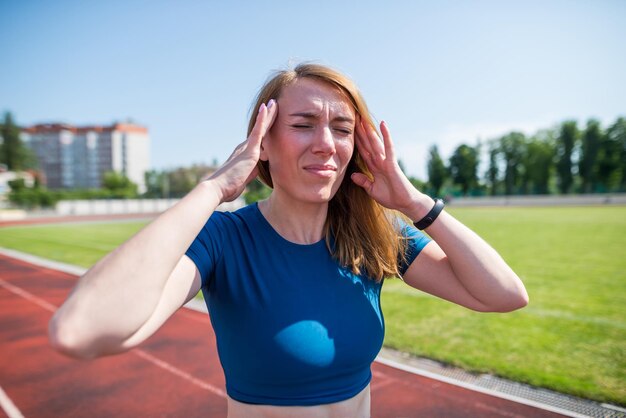 Maux de tête chez une coureuse Une femme souffre de maux de tête ou de symptômes de maladie en courant sur un tapis roulant