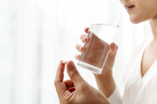 Maux de tête des femmes tiennent un médicament avec un verre d&#39;eau