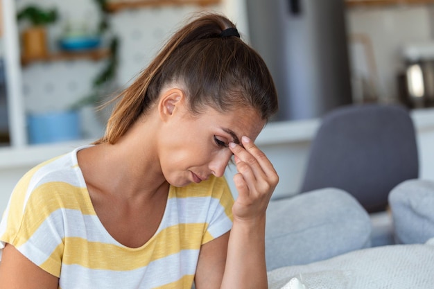 Maux de tête Gros plan photo d'une jeune femme qui est assise sur un canapé en touchant sa tête tout en souffrant d'une migraine