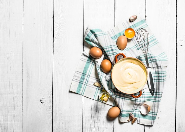 Mayonnaise fraîche avec les ingrédients. Sur une table en bois blanche.