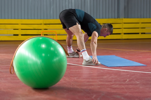 Mec athlétique en vêtements de sport et fitness tracker faisant des exercices dans la salle de gym.