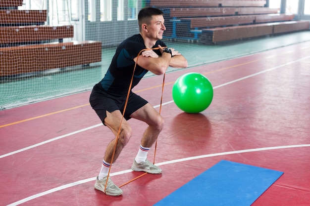 Mec athlétique en vêtements de sport et fitness tracker faisant des exercices dans la salle de gym.