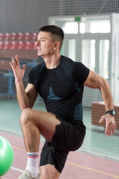 Mec athlétique en vêtements de sport et fitness tracker faisant des exercices dans la salle de gym.