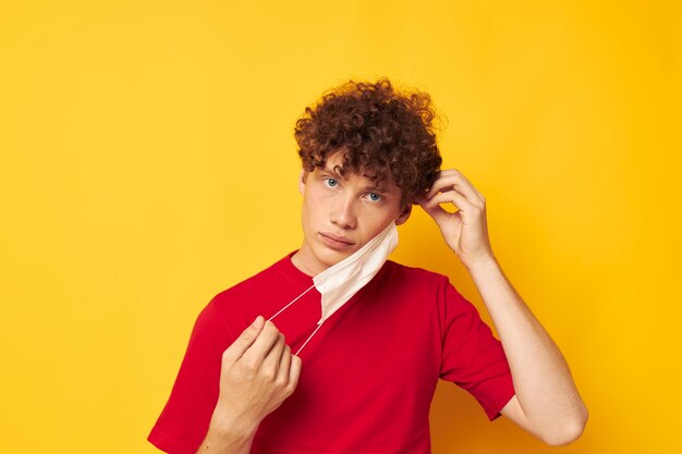 Mec aux cheveux bouclés rouges dans un t-shirt rouge masque médical protection fond jaune inchangé