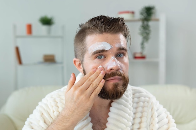 Mec barbu appliquant une crème pour le visage devant un miroir de soins de la peau et un concept de spa pour homme