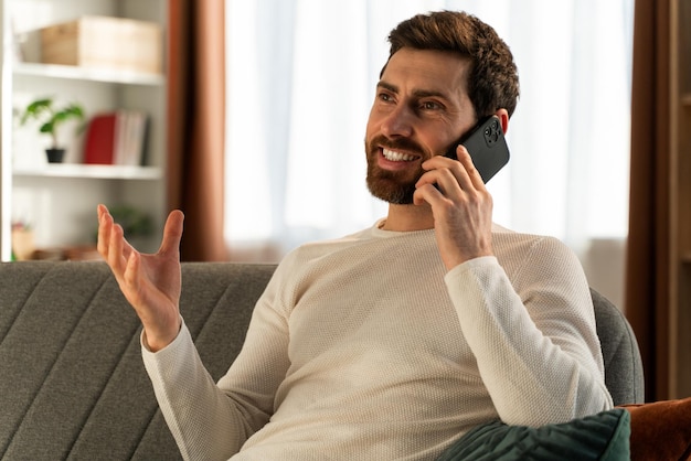 Mec barbu portant des lunettes souriant à la caméra et discutant sur son smartphone. Stock photo