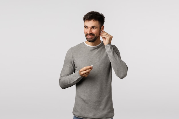 Mec barbu en pull gris mettant des écouteurs sans fil